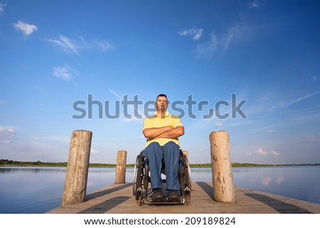 handicapped man on a wheelchair on wooden boardwalk with crossed arms