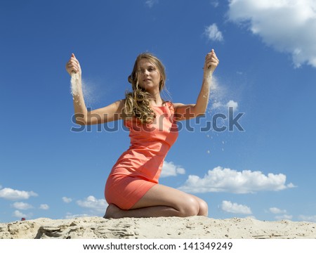 20 years old blond-haired girl on knees strewing sand through fingers