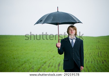 Handsome young businessman with umbrella outside -protection concept