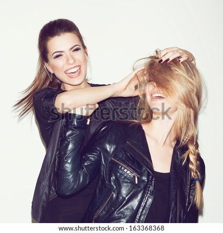 Two young girl friends having fun and smiling. Brunette making hairdo to blonde