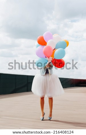 Jumping girl with colorful balloons in her hand. Warm sunny day. Outside.