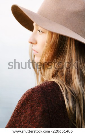 Closeup portrait of blonde girl standing outside. Profile to camera. Wearing hat and jacket.