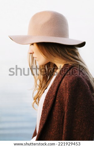 Closeup portrait of a pretty blonde girl walking down lakeside. Profile to camera. Wearing hat and jacket. Outside