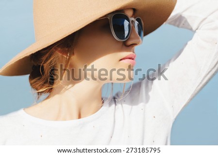 Portrait of young beautiful blonde girl wearing hat and sunglasses. Shadow on her face. Outside