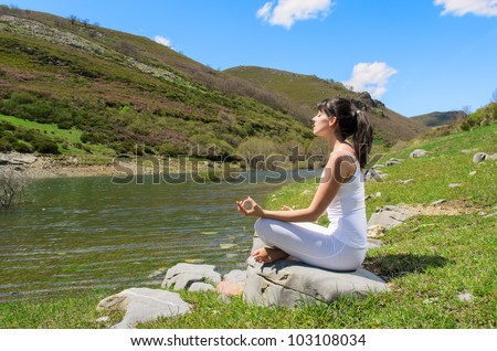 Woman doing yoga breathing exercises on nature. Caucasian young woman in white relaxing near a mountain river.
