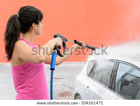 Young woman cleaning and washing silver car with water jet.
