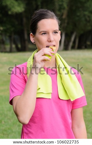 Young woman eating energy bar outside in a park. Caucasian young athlete.