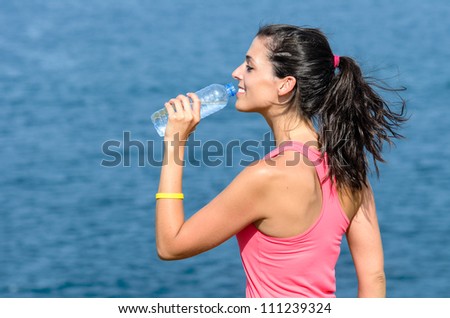 Woman drinking water on sea background after exercising. Fitness beautiful caucasian model.