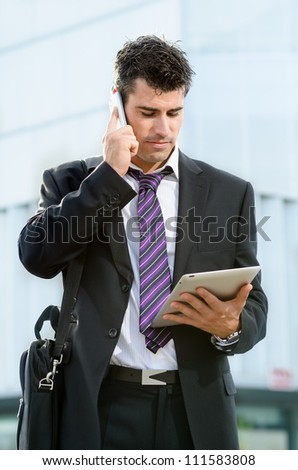 Busy businessman with cell phone. Man looking tablet making business call outdoor. Handsome caucasian male model.
