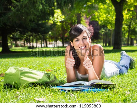 Student in park with thumbs up. Happy university woman student stufying outdoor lying on grass. Copy space.