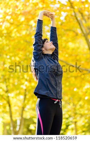 Caucasian sportswoman stretching and doing aerobic exercising outdoor. Autumn blur golden trees on background.