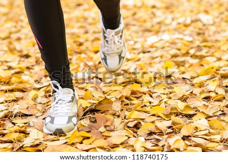 Woman running concept. Runner feet on autumn leaves ground. Female athlete exercising outdoor.