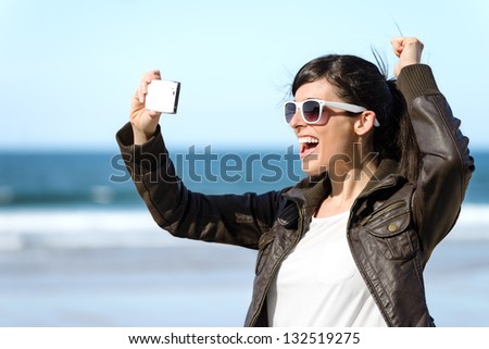 Fun woman video call on cellphone. Playful happy girl on vacations taking self photo on sea background at the beach.