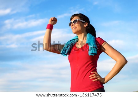 Happy successful fitness woman raising arm with energy and fist to the sky after running and exercising. Sport  goals and achievements concept. Caucasian beautiful female athlete in sportswear.