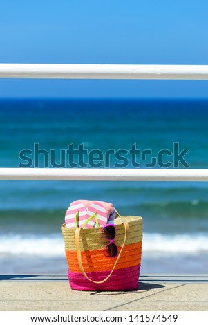 Summer handbag with beach items against the sea on bright hot day.