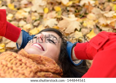Happy woman on autumn season relax. Brunette girl lying down and smiling on fall golden leaves in park. Tranquility and peace concept.