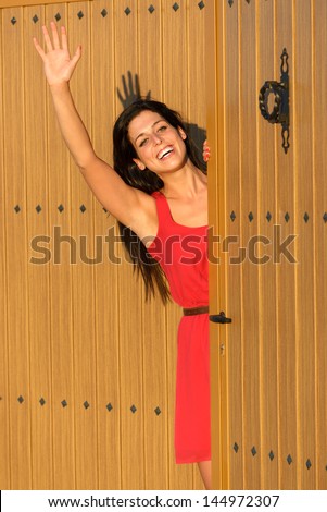 Happy woman waving and opening country house door to welcome guests visitors. Charming caucasian brunette girl good bye standing in home entrance.