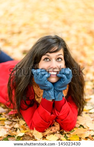 Nervous happy woman on autumn day thinking and looking up. Naughty girl surrounded by golden fall leaves lying down and smiling. Temptation or decision concept.