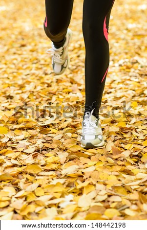 Running and sport on autumn concept. Female runner legs detail training on ground full of fall leaves.