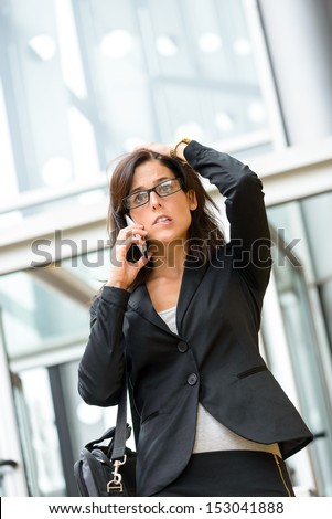 Upset stressed businesswoman on cellphone. Anxious woman on business crisis receiving bad financial news outside city corporate building. Hispanic female executive suffering stress and anxiety.