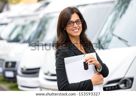 Successful female sales representative in van transport trade fair. Commercial exhibition and rental vehicle concept. Beautiful female seller or salesman holding car keys.
