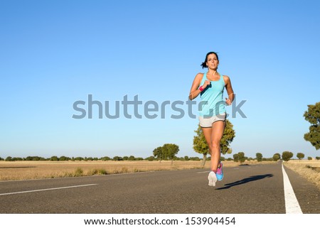 Fitness woman running fast in rural straight road. Runner exercising and training hard for marathon. Full body sport scene with copy space.