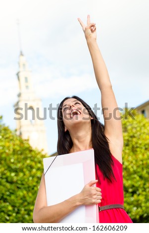 College female student raising arm after passing exams with success. Happy girl in university campus.