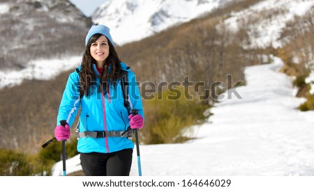Woman hiking in winter mountains. Female hiker walking on a snow covered track wearing warm sport outfit.