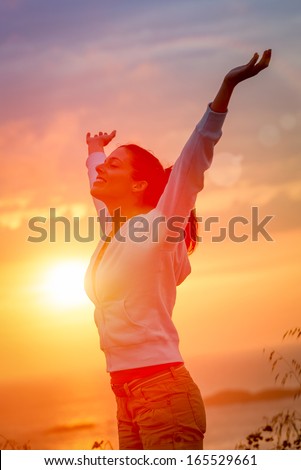 Woman enjoying freedom and life on beautiful and magical sunset. Blissful girl raising arms feeling free, relaxed and happy.