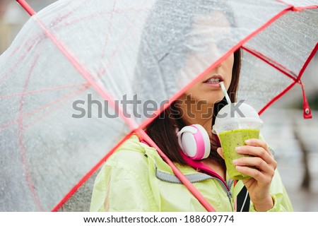 Fitness woman drinking vegetable detox smoothie after workout. Sportswoman sipping healthy drink with straw on rainy day.