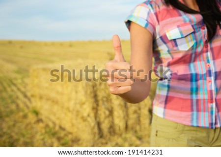 Agriculture business success concept. Female farmer with thumbs up for approving gesture on country rural field background.