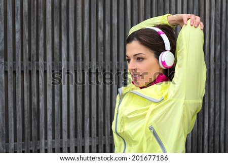 Urban fitness woman stretching arms triceps on fitness working out and exercising outside. Sporty woman exercising outside wearing headphones and outfit sportswear.