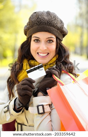 Fashion trendy woman showing credit card and carrying shopping bags after buying on autumn. Caucasian brunette shopper spending money in clothes.