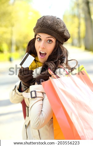Fashion trendy woman showing credit card and carrying shopping bags after buying in autumn. Amazed shopper jaw dropping.