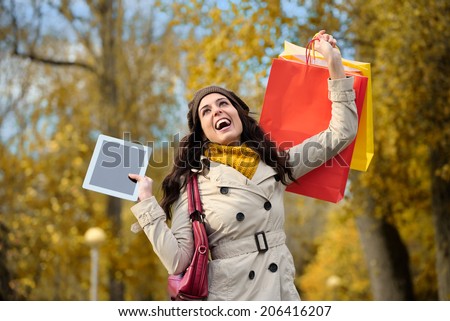 Joyful fashion woman raising shopping bags and digital tablet in autumn. Successful female shopper having fun.