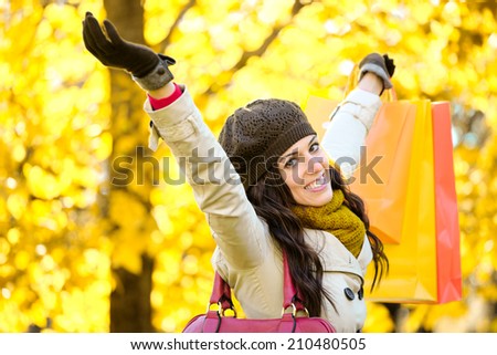 Blissful woman raising shopping bags  and arms while having fun buying in autumn. Successful female shopper outside in fall season.