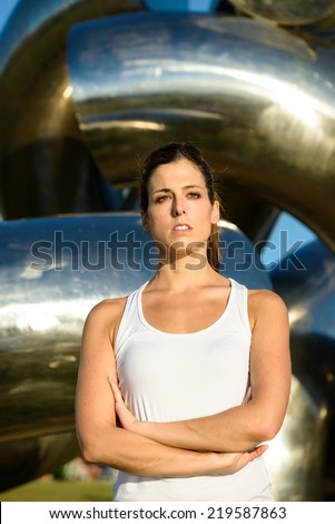 Focused serious female athlete with arms crossed looking motivated. Fitness woman on outdoor summer sunset workout.