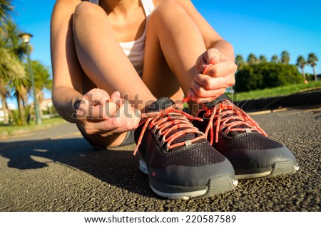 Female athlete lacing running footwear and getting ready for outdoor workout. Woman exercising in a park on summer.
