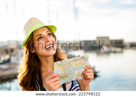 Joyful beautiful tourist looking tourism guide map at sport harbor of Gijon, Asturias, Spain. Woman enjoying summer vacation travel.