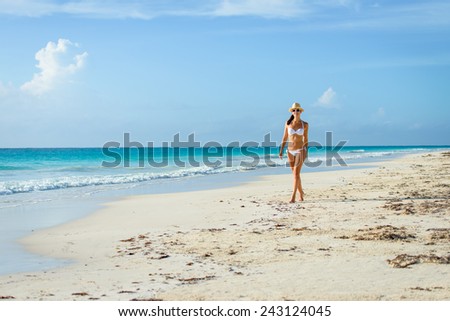 Tanned woman in white bikini enjoying idyllic tropical beach and caribbean summer vacation. Beautiful young tanned brunette enjoying a walk by the sea at Playa Paraiso, Riviera Maya, Mexico.
