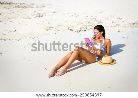 Relaxed woman reading a book at the beach during summer vacation. Young happy brunette lying on the sun with a e-book