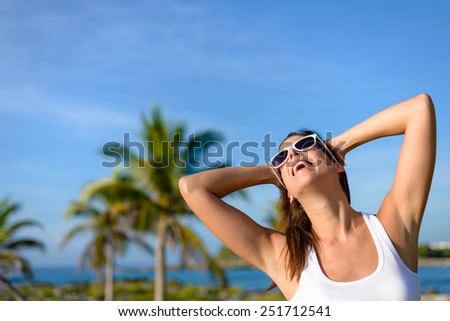 Happy woman on tropical travel having fun. Caribbean vacation joy and freedom. Caucasian brunette model wearing sunglasses and looking up to clear blue sky.