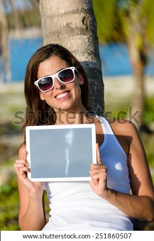 Brunette woman on tropical vacation holding digital tablet. Touch pad screen for copy space frame. Caribbean travel concept.