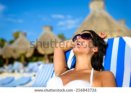 Joyful woman at tropical resort caribbean beach resting on outdoor chaise lounge. Summertime vacation tourism and travel concept. Beautiful brunette sunbathing and relaxing at Mayan Riviera, Mexico.