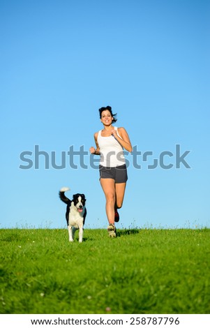 Woman and dog running and exercising outdoor in grass field on summer or spring. Happy female athlete training with her pet.
