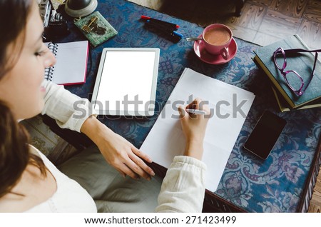 Working at home concept. Entrepreneur business woman writing and taking notes using her digital tablet on retro desk full of objects.