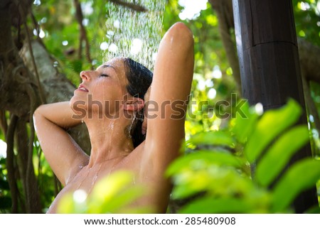 Relaxed happy woman taking spa shower outdoor in exotic garden.