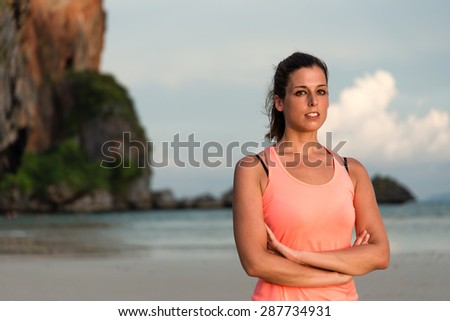 Fitness woman portrait. Motivated female athlete with arms crossed at the beach, Krabi, Thailand.