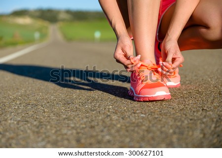 Running challenge concept. Female athlete tying sport footwear laces on road before training.