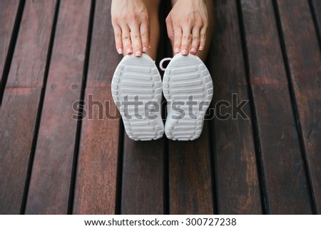 Fitness lifestyle and sport concept. Sporty footwear and female hands close up. Woman stretching legs outdoor on wooden floor.